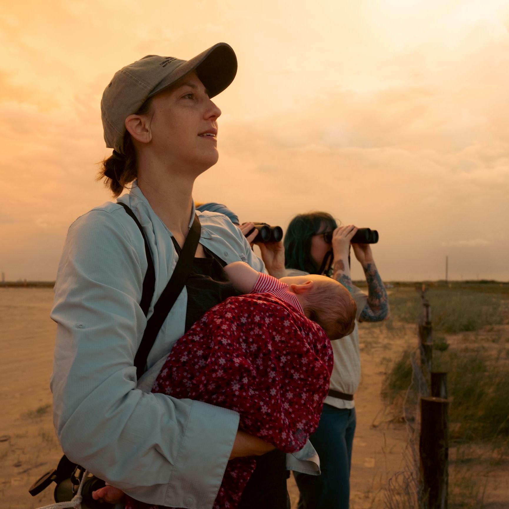 A young lady looking out into the distance while standing with her back to the sunset