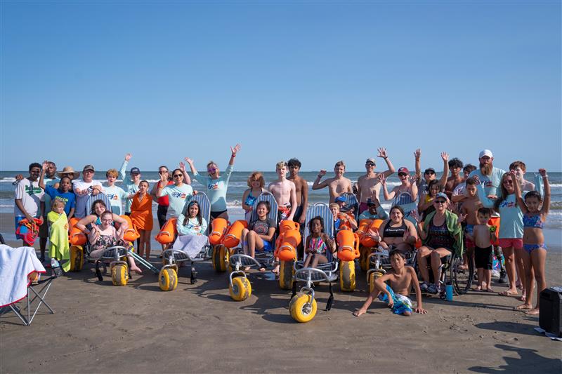 Group of people at the beach utilizing beach wheelchairs